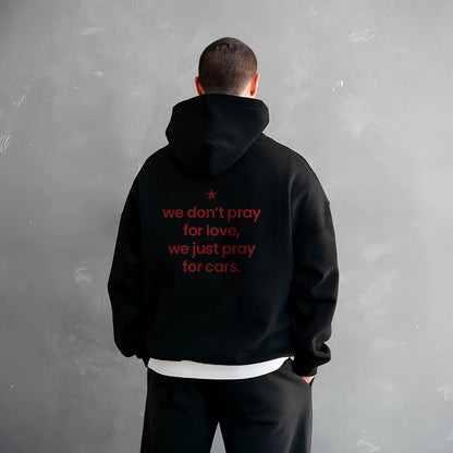 Oversized black hoodie streetwear with red text 'we don't pray for love, we just pray for cars' on the back